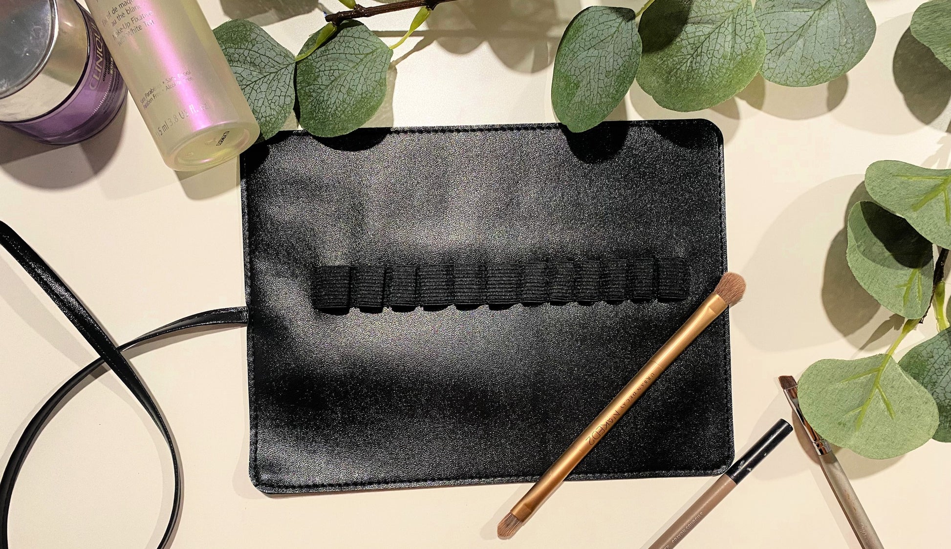 inside of  black travel make up brush set with holders for brushes on white background and green leaves
