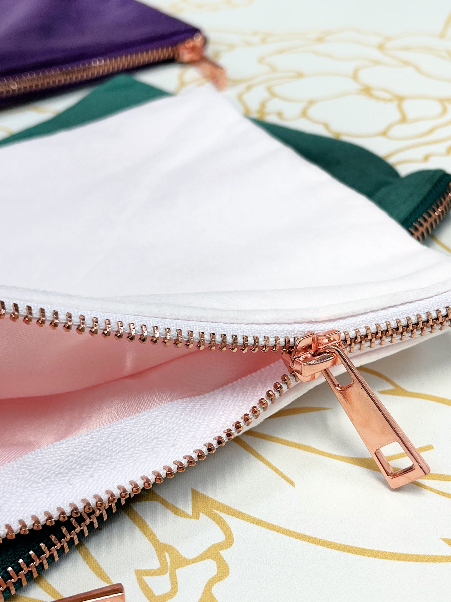 close up to velvet blush make up case with rose gold zipper pink satin liner with green and purple make up case in background