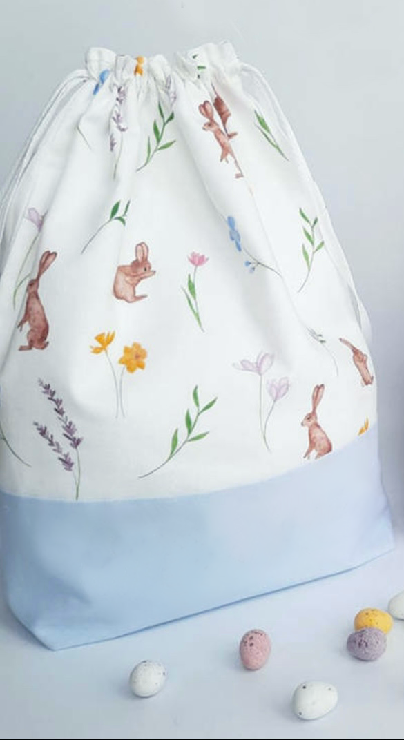 Blue drawstring Easter Bunny Bag with rabbits flowers leaves on white background and candy eggs