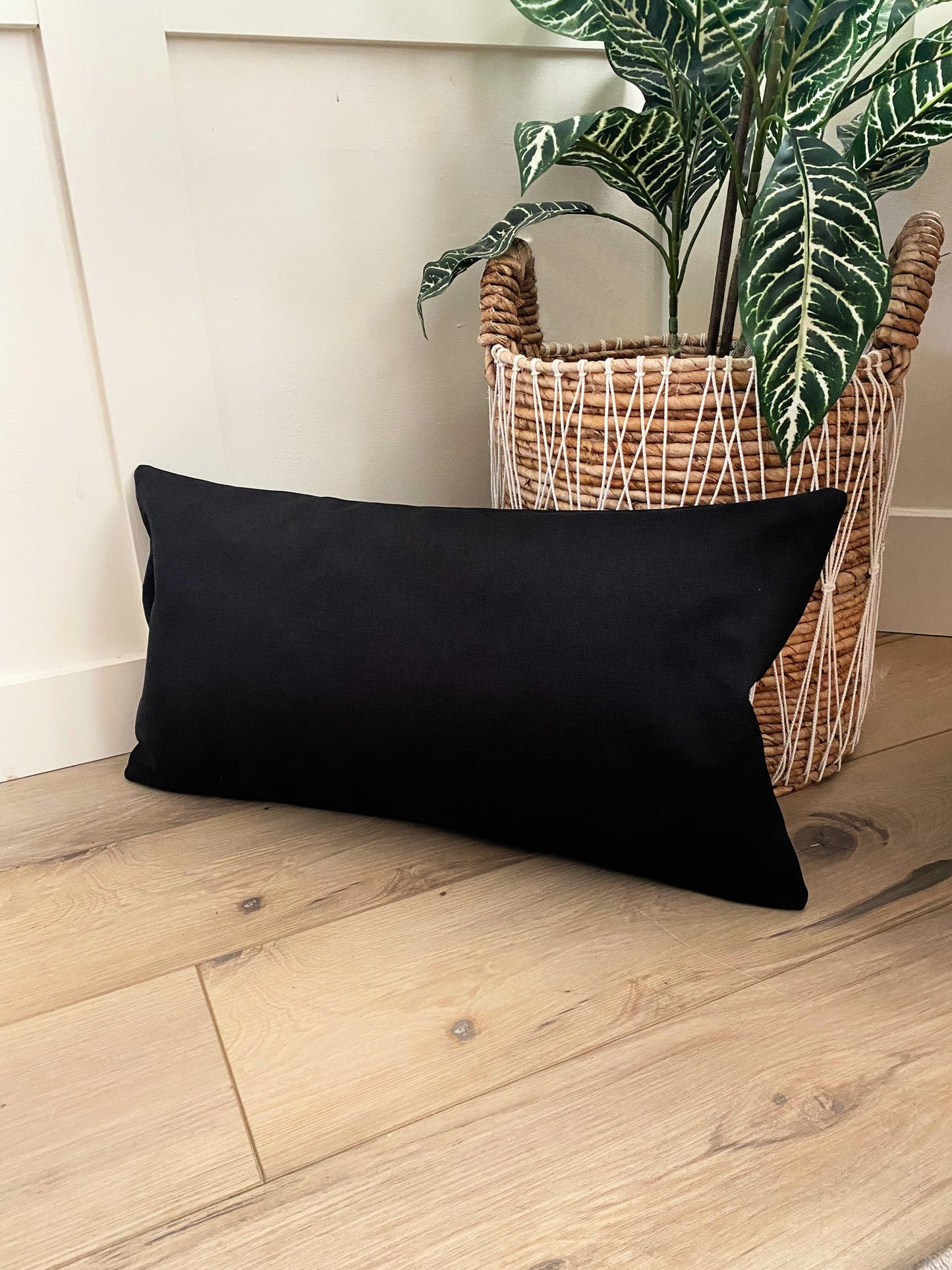 blank black lumbar pillow for sublimation or htv on wood floor infront of fake tree in whicker basket