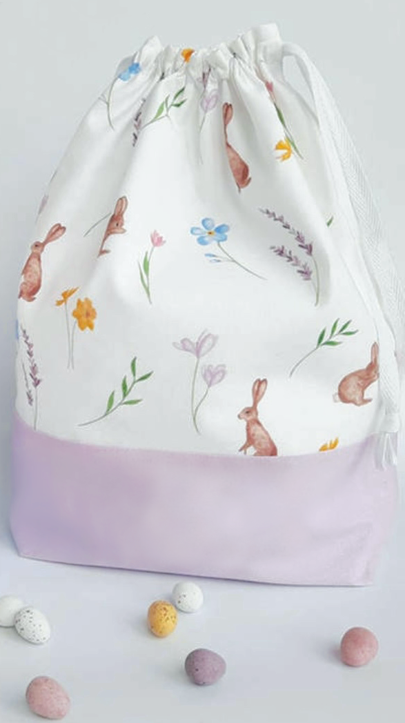 lilac drawstring Easter Bunny Bag with rabbits flowers leaves on white background and candy eggs