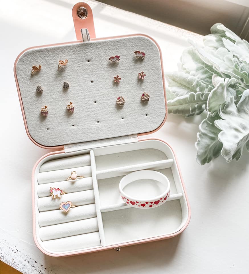 inside of square pink jewellery case with earrings rings and bracelets on white desk with greenery