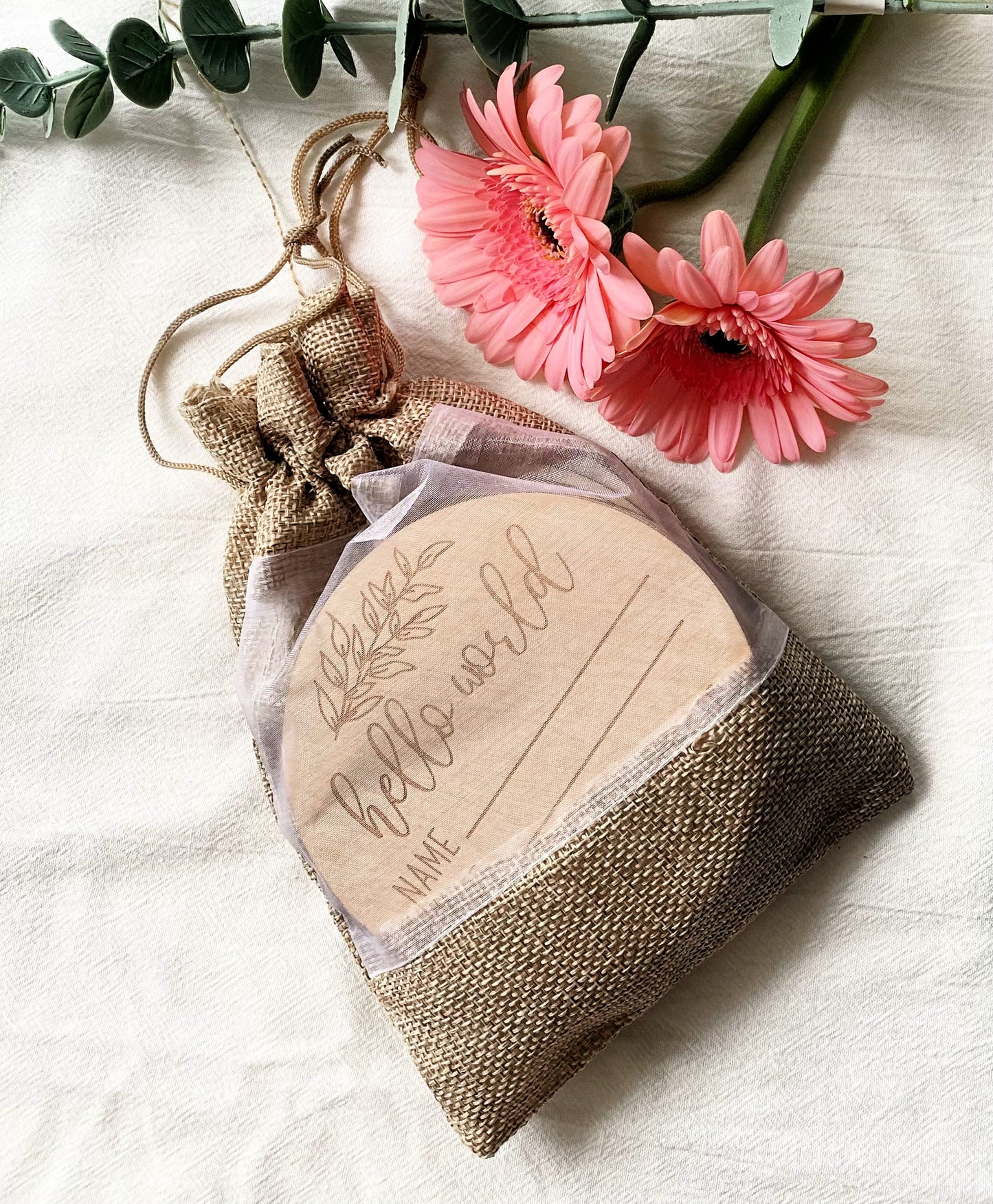 birth announcement wood piece hello world in jute bag with white background and pink flowers