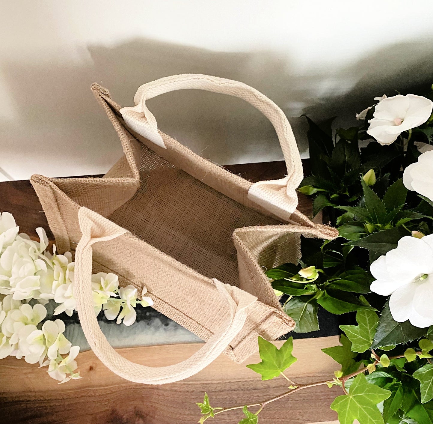 inside of open jute bag with handles on wood table with white flowers 