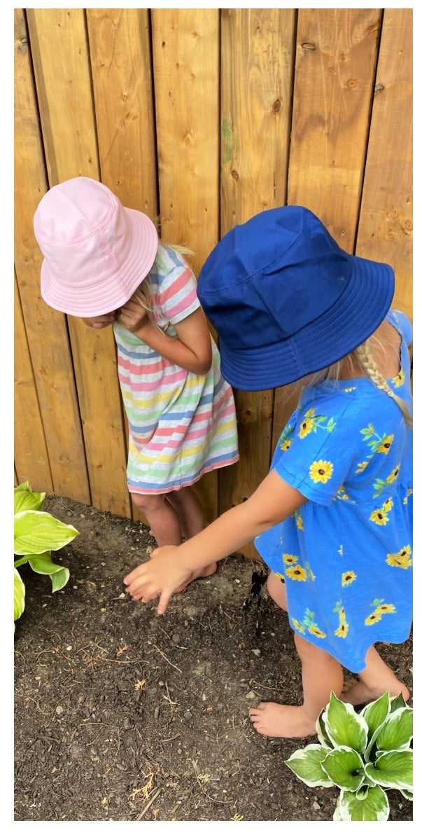 two girls in garden wearing sundress pink and blue bucket kids hats 