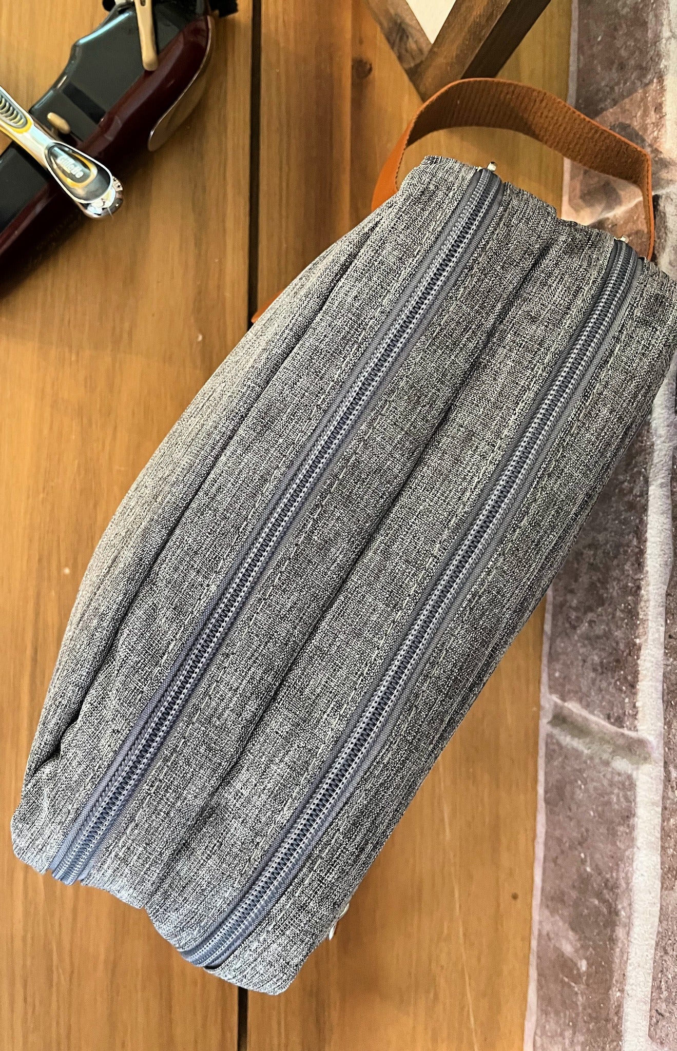 top of grey shaving bag showing two zippered compartments on wood table with razor and brick background