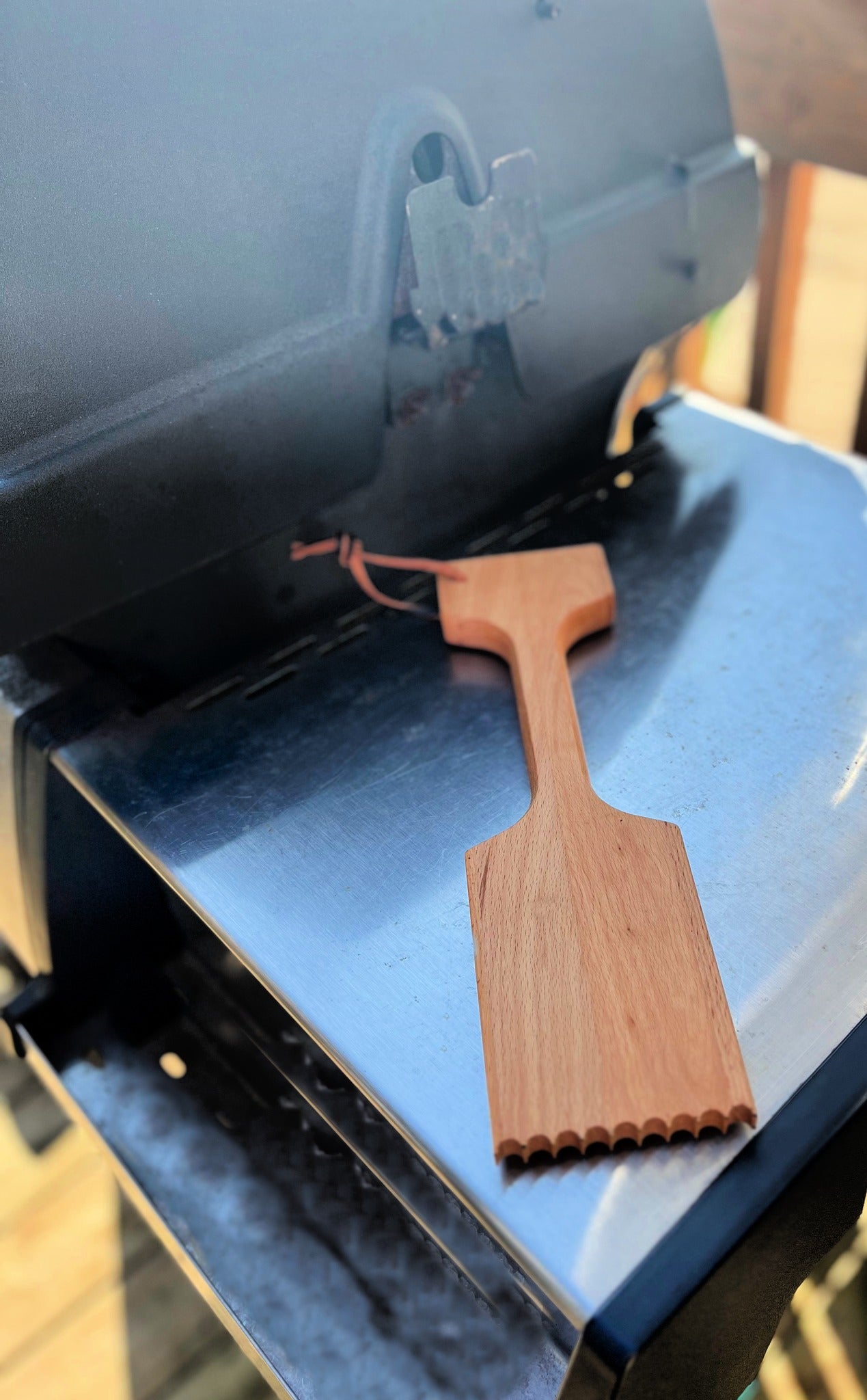 wood bbq scrapper with handle on edge of bbq outside