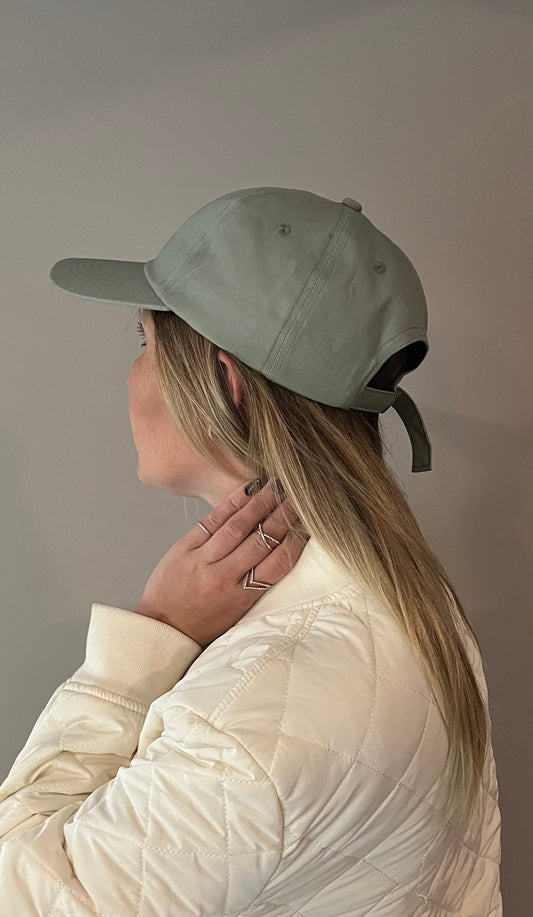 women wearing white spring coat wearing rings with sage baseball dad style hat infront of grey background