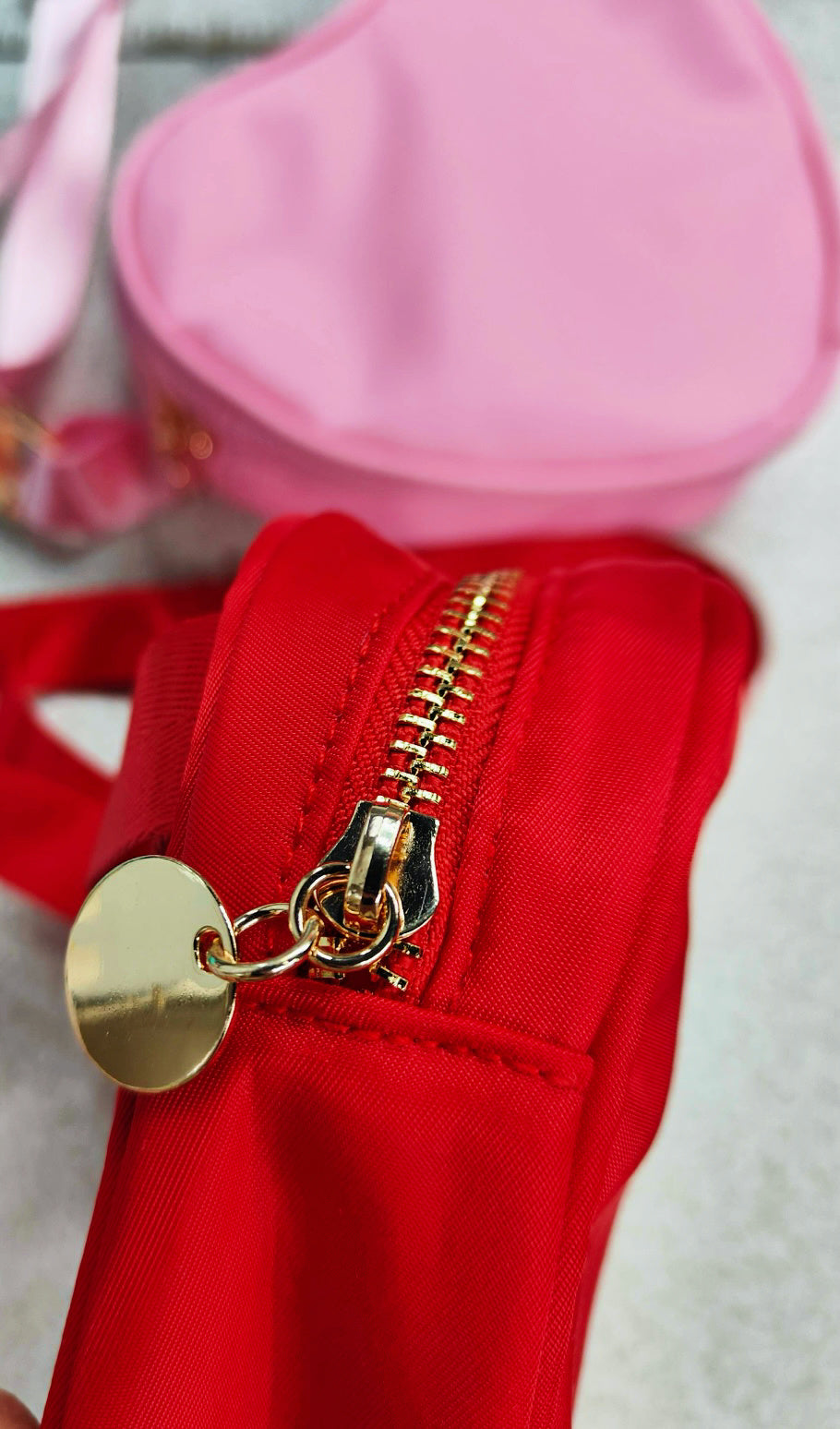 red heart bag showing gold zipper with gold circle and light pink bag in the background