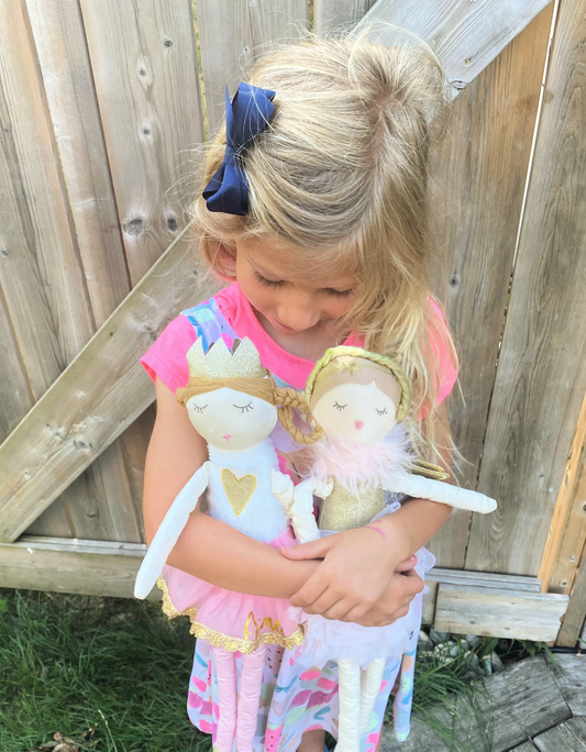 girl holding soft ballerina dolls with braids outside by wooden gate