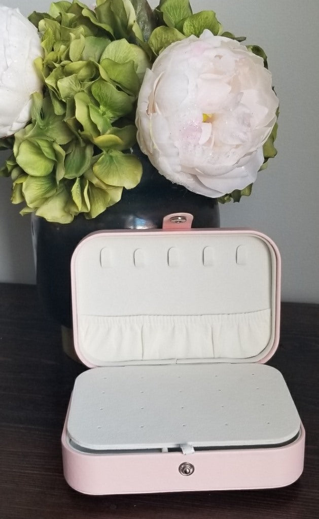 open rectangle pink jewellery case on desk with vase of flowers and greenery 