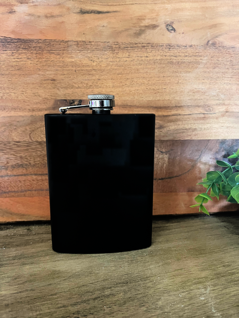 black 8oz flask on wood background with green leaves