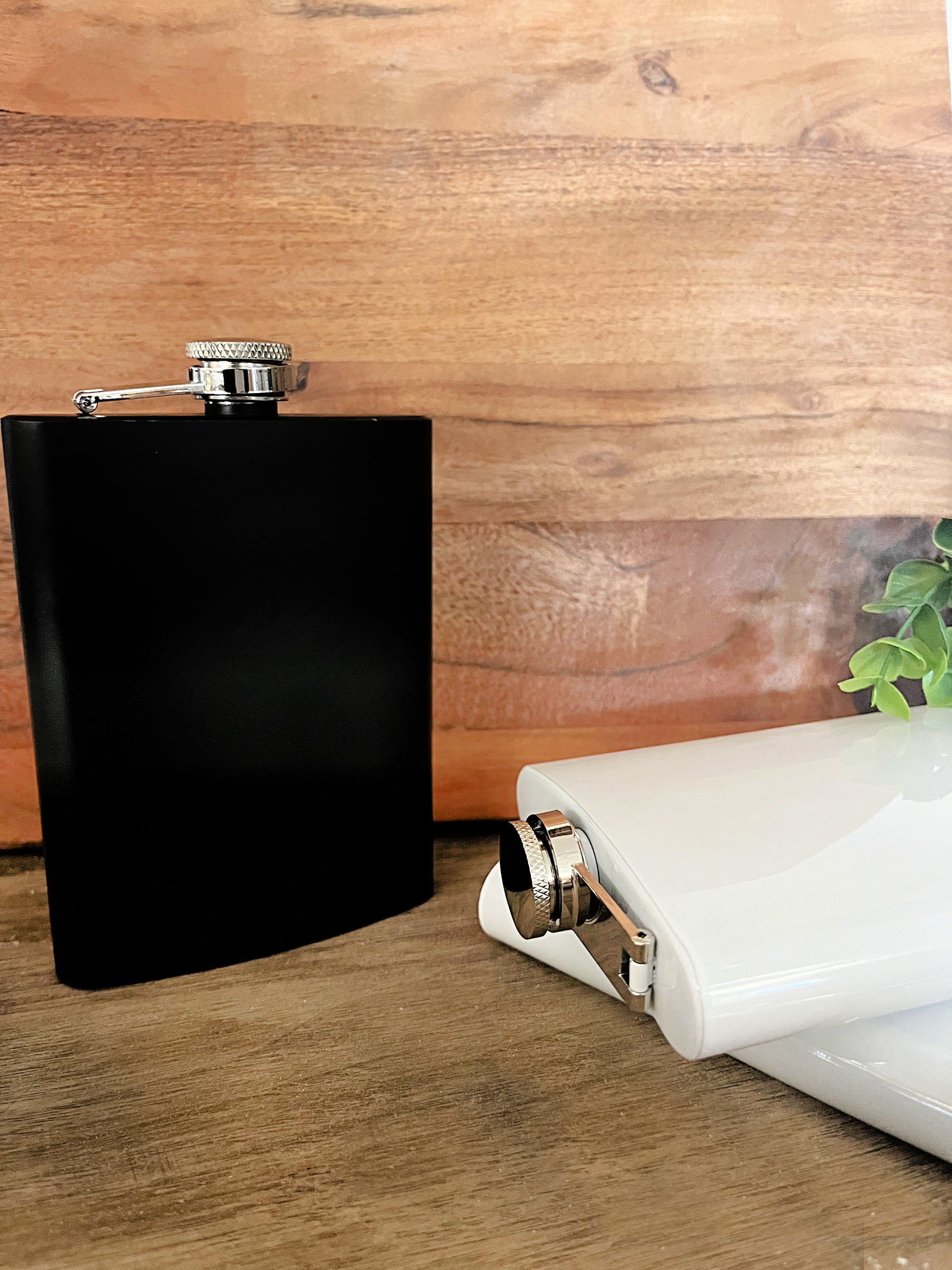 black and white stainless steel 8oz flasks on wood background with green leave