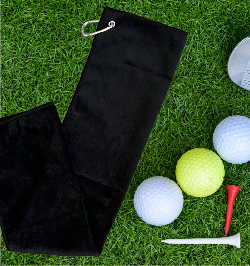 black golf towel with clip on grass with golf balls and tees