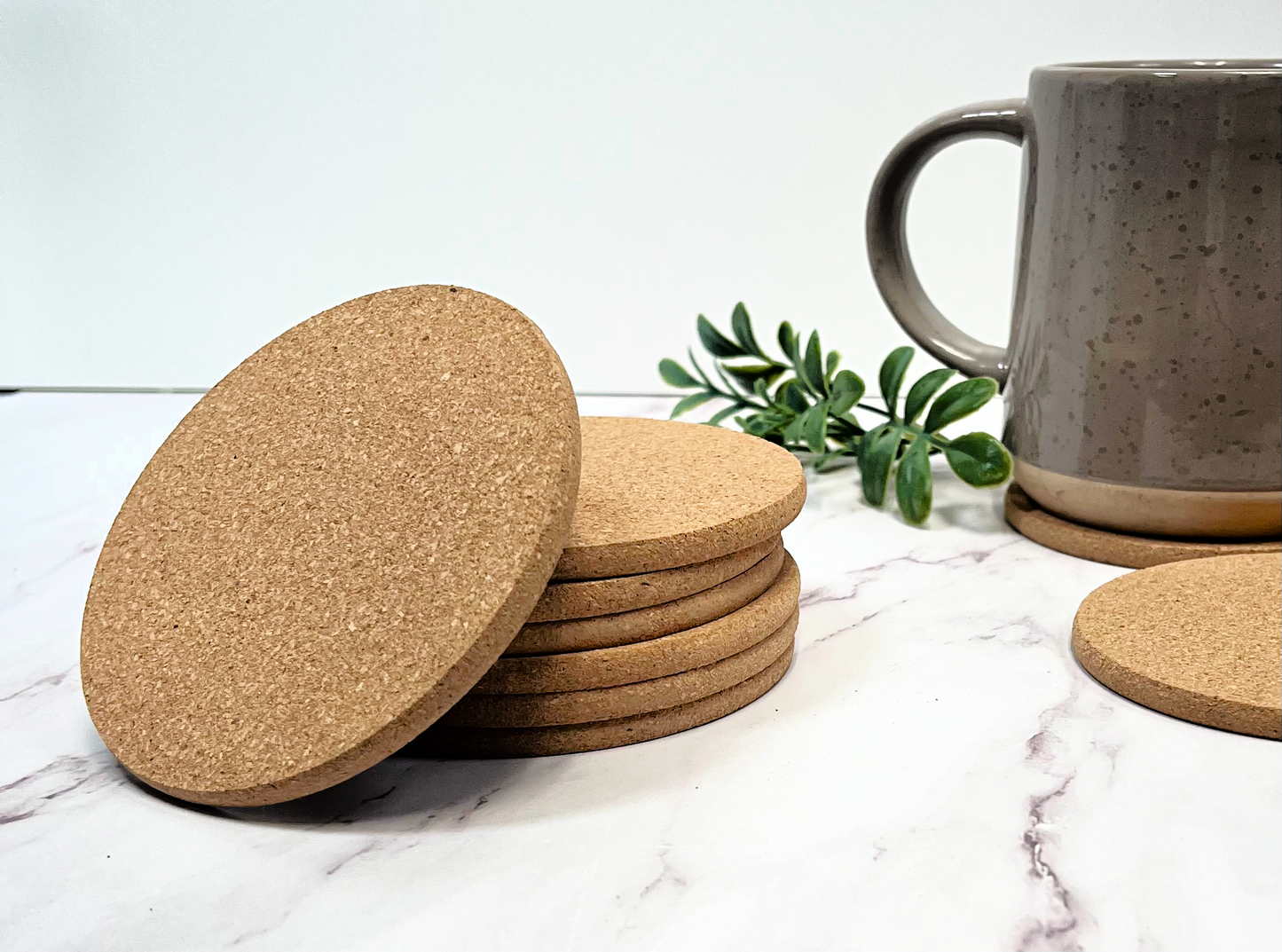 stack of cork coasters on marble table with clay handle mug and green sprig