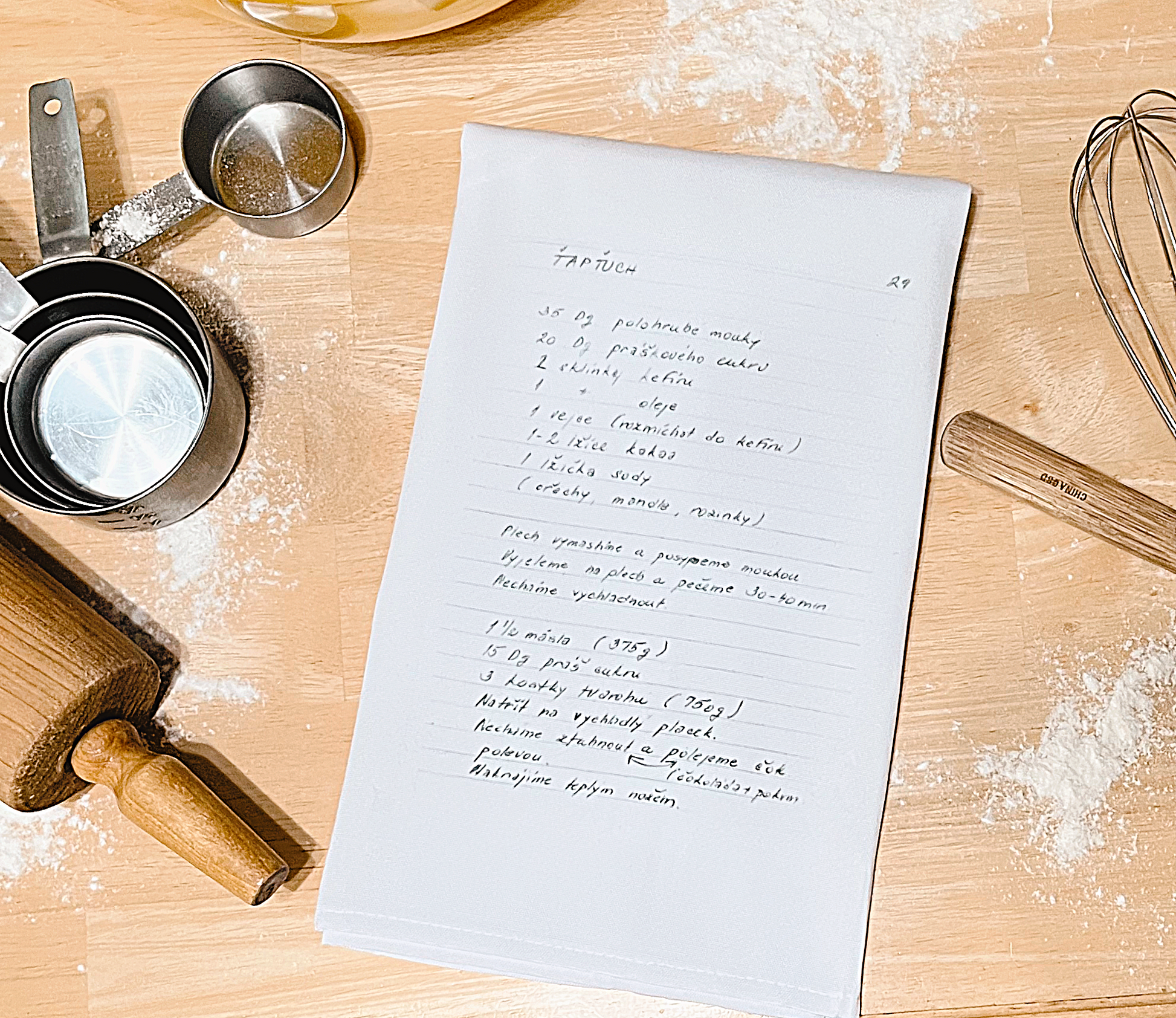 white tea towel with recipe on table with measuring cups rolling pin whisk and spoon