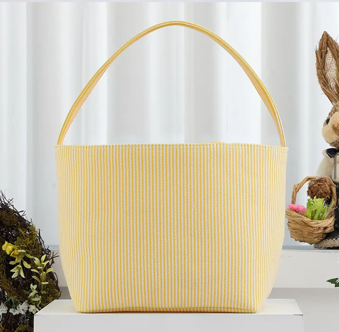 yellow striped seer sucker Easter basket with handle on white stand with wreath and rabbit in background 