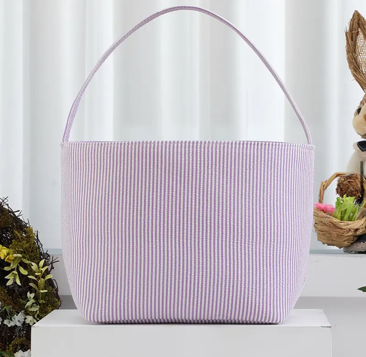 Purple striped seer sucker Easter basket with handle on white stand with wreath and rabbit in background 