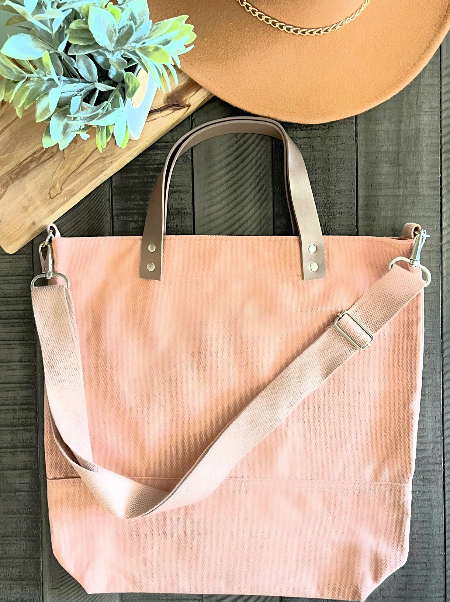 pink bag with leather handle pink strap on wood background with tan hat and green leaves