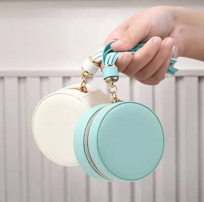 white and Seafoam round jewellery case with golf zipper and tassels being help by the hassle against white background