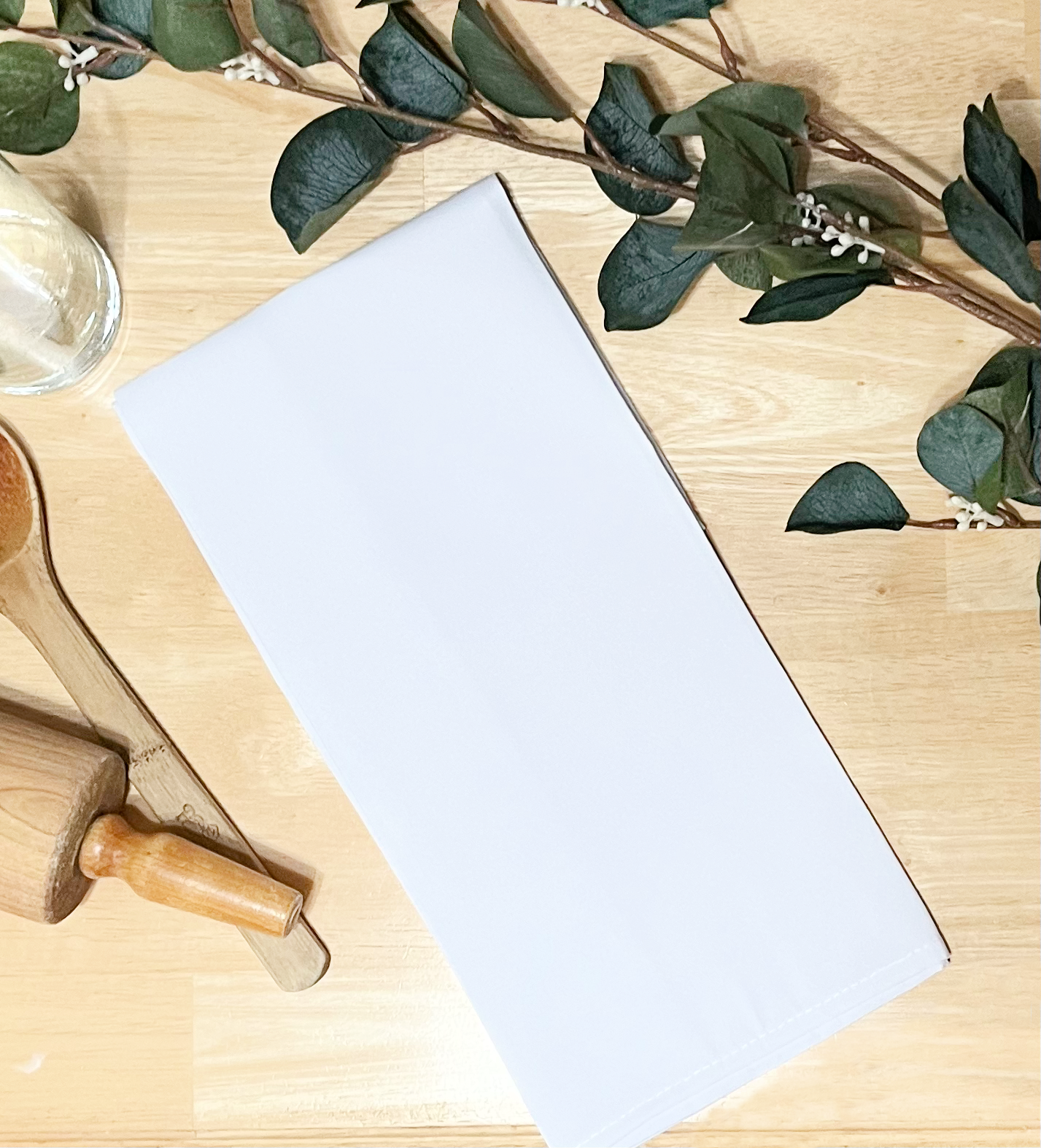 white tea towel on wood background with rolling pin spoon and greenery