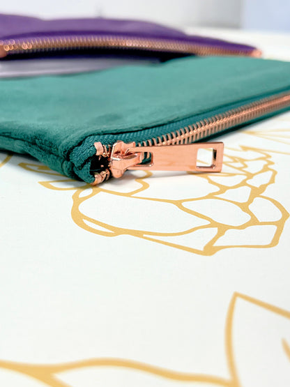 close up to closed green velvet make up bag with rose gold zipper on flower background