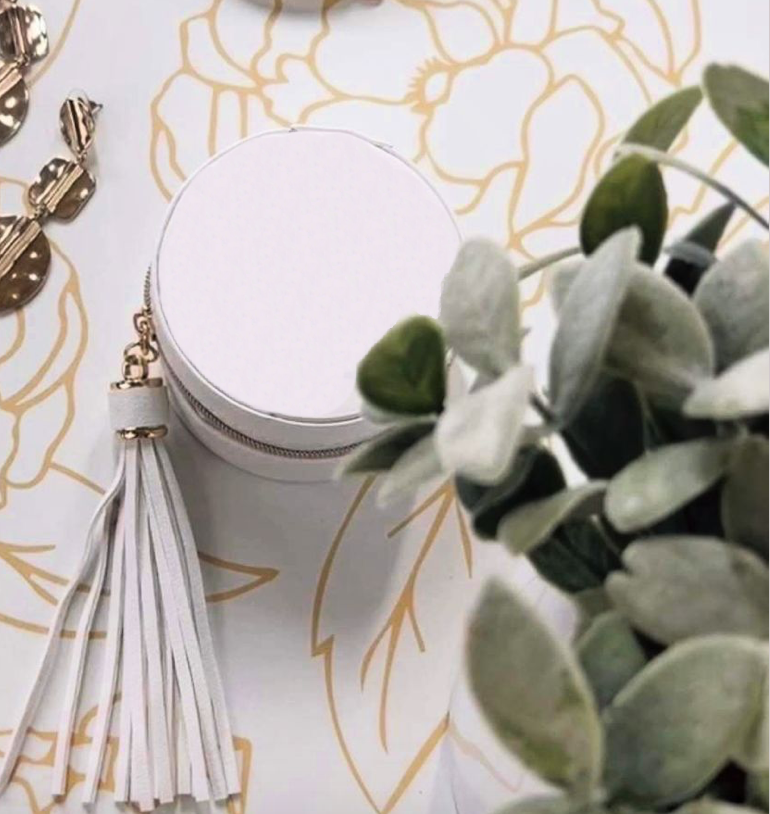 white round jewellery case with gold zipper white tassel on flower background with earrings and plant