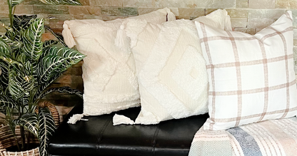 accent pillow cases with tassels and brown checkered on black bench beside fake tree and brick background