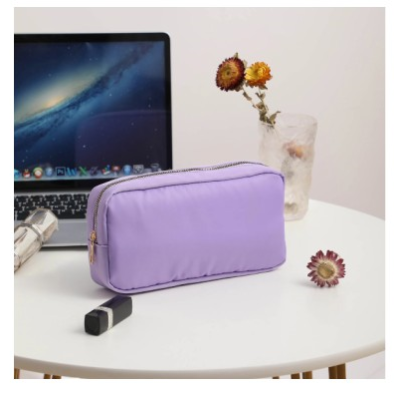 purple makeup pouch with gold zipper on white table and laptop and make up