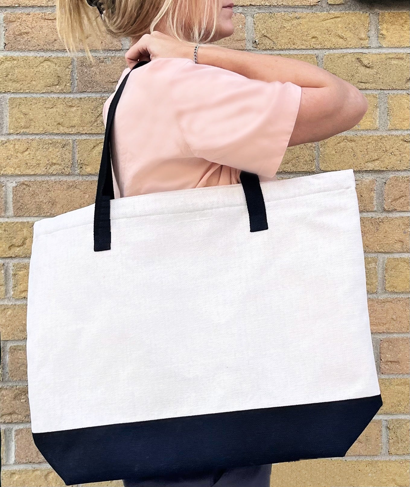 pink shirt carry all tote back on brick background, white canvas bag with black bottom and handle