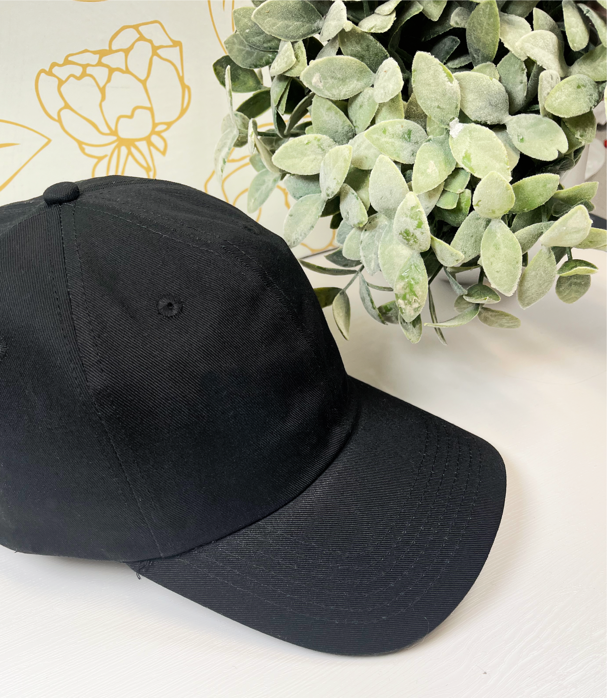 black dad style women's baseball hat on white table by greenery