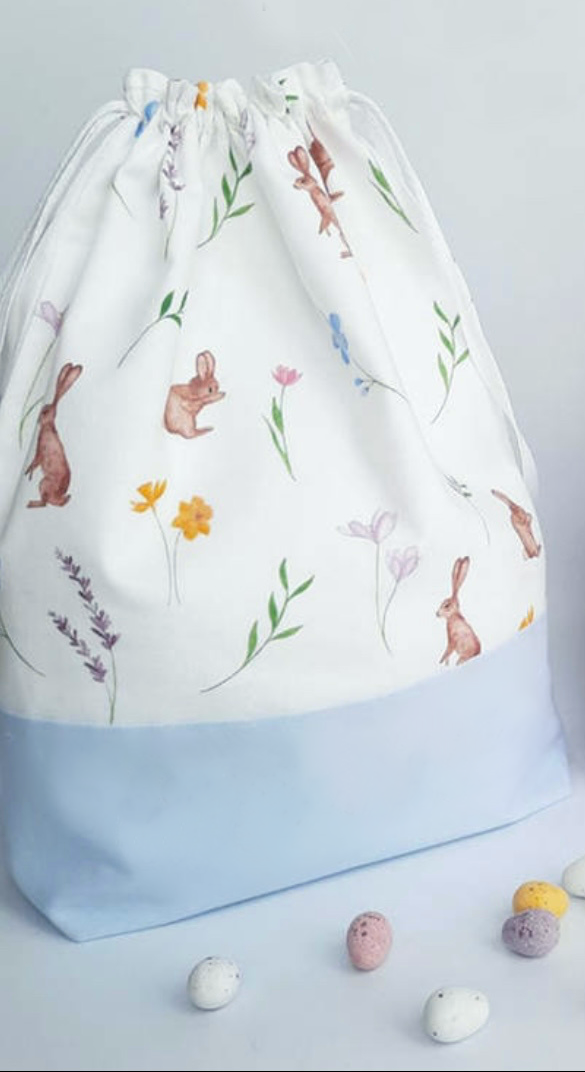 Blue drawstring Easter Bunny Bag with rabbits flowers leaves on white background and candy eggs 