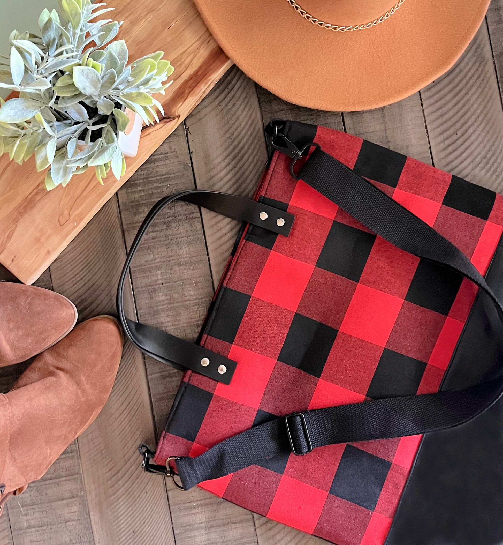 leather handle buffalo plaid bag on wood background with brown boots hat and plant