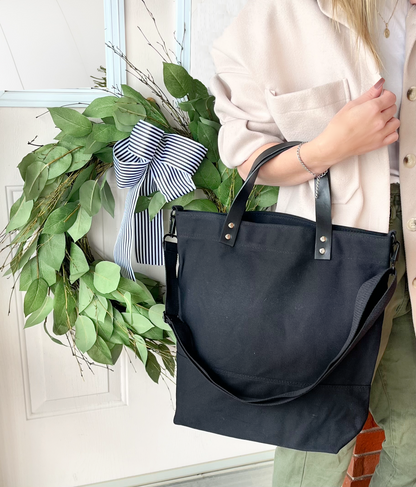 leather handle black canvas bag with handle and strap against green pants blush jacket green wreath