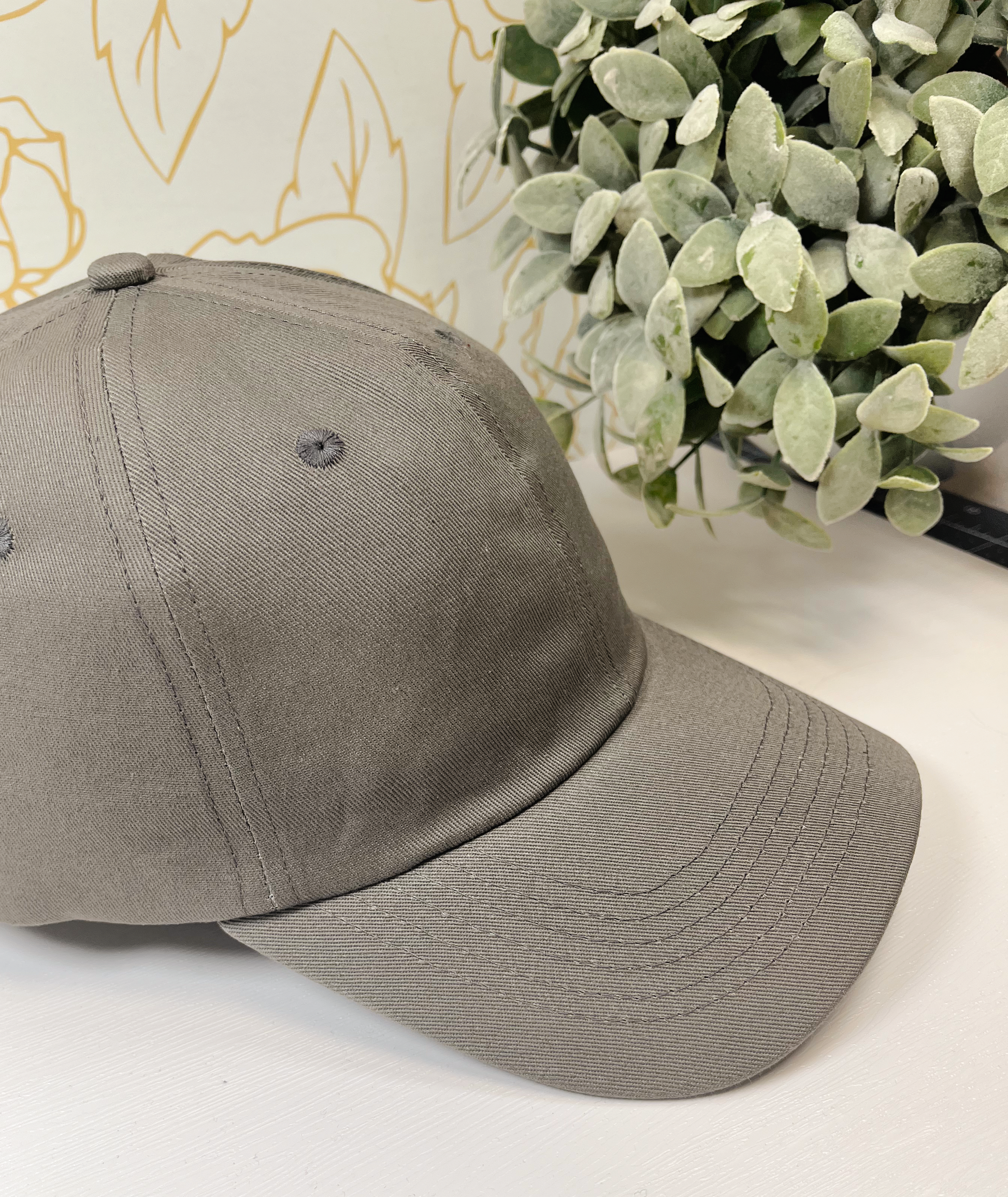 grey metal dad style women's baseball hat on white table by greenery