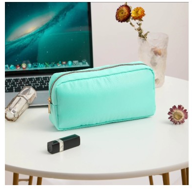 mint makeup pouch with gold zipper on white table and laptop and make up