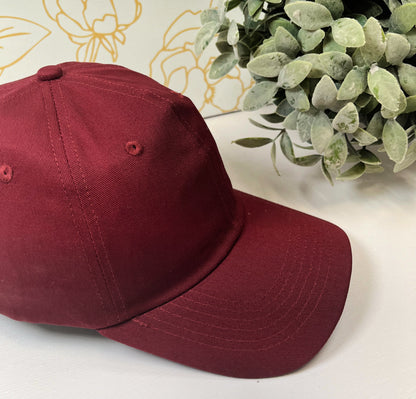 marron dad style women's baseball hat on white table by greenery