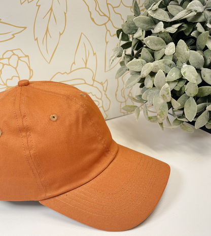 burnt orange dad style women's baseball hat on white table by greenery