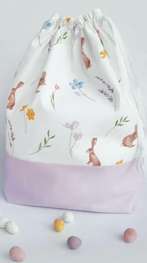 lilac drawstring Easter Bunny Bag with rabbits flowers leaves on white background and candy eggs 