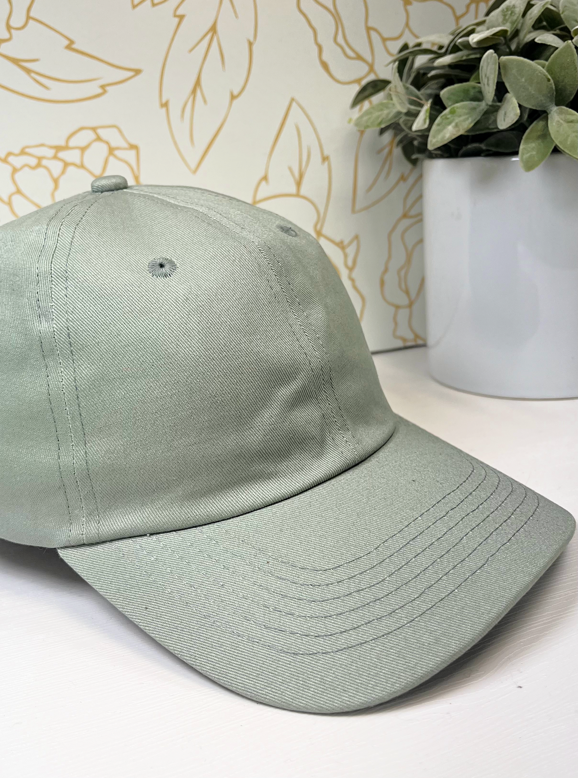 sage dad style women's baseball hat on white table by greenery