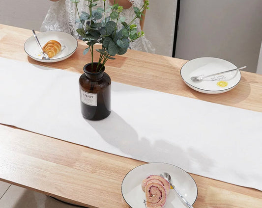 white table runner on wood table with vintage glass jar and greenery and plates with desserts