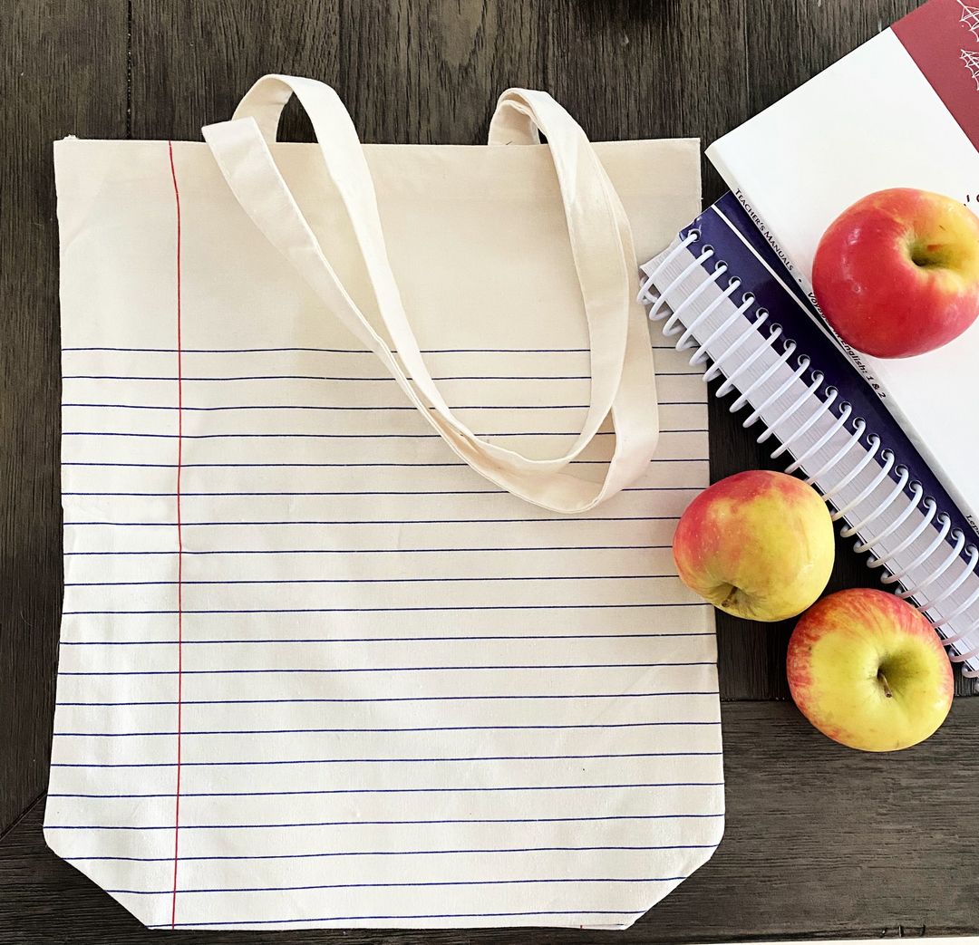 lined teacher tote on wood background with text books and apples