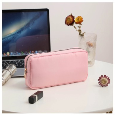 pink makeup pouch with gold zipper on white table and laptop and make up