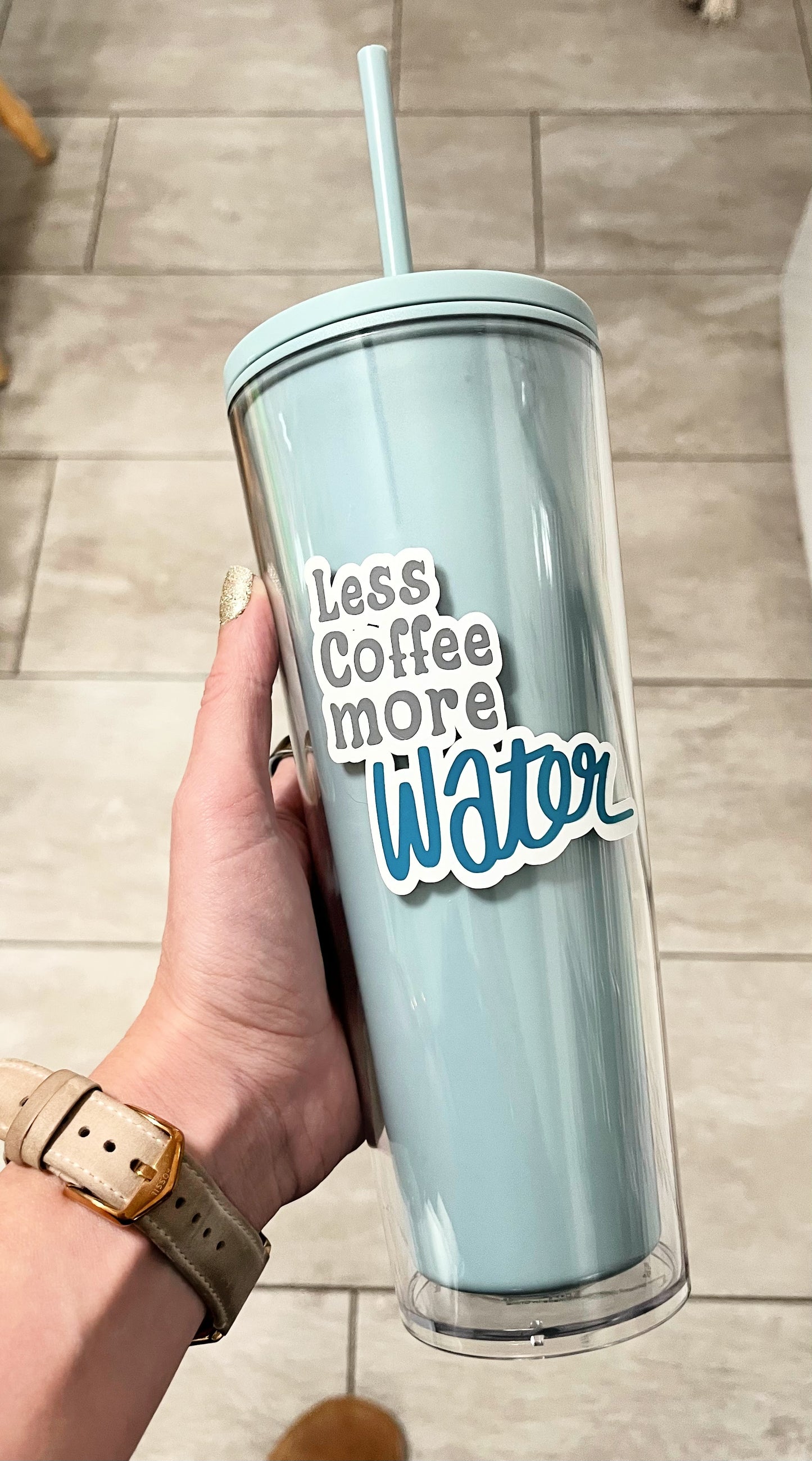 24oz acrylic tumbler with blue and clear says less coffee more water on the cup held on tile background 