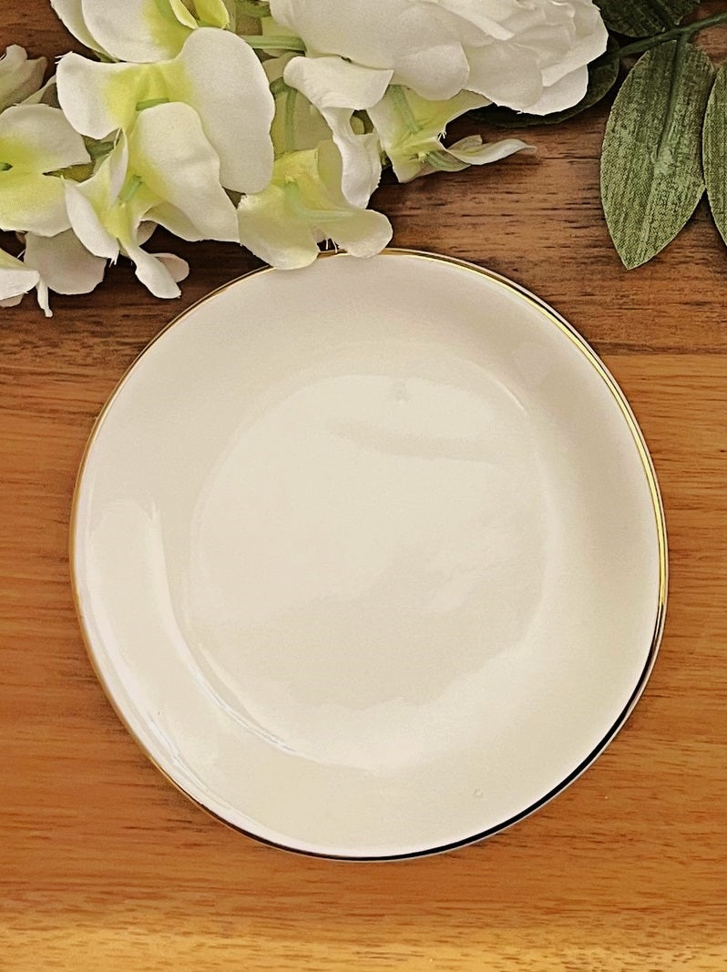 white gold rimmed ring dish on wood background with leaves and white flower